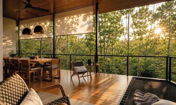 A wooden deck with a dining area, seating, and a view of a forest. - Casa Aloha Montezuma (Cobano)