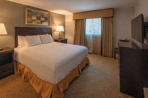 A hotel room with a large bed, a desk with a computer, a TV, and a window with curtains.