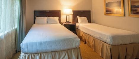 Ein Hotelzimmer mit zwei Betten, einem Nachttisch mit Lampe und zwei gerahmten Bildern an der Wand.