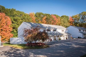 A two-story white building with a covered driveway and a small tree in front.