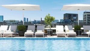 A rooftop pool with white lounge chairs and umbrellas, a city skyline in the background, and a clear blue sky. - Luxury Apartment w King Bed, Shared Pool & Rooftop (Cambridge)