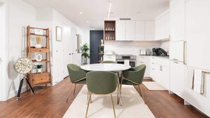 A modern kitchen with white cabinets, a round dining table with green chairs, and a wooden sideboard with a clock.