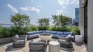 A rooftop patio with a sectional sofa, round tables, and potted plants.