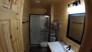 Een kleine houten badkamer in een cabin, met douche, toilet en wastafel.