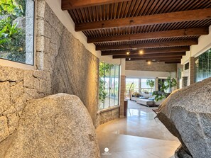 A modern interior with a stone wall, wooden ceiling beams, and a glass door leading to an outdoor area. - Casa Garopaba Vista Panorâmica do Mar (Garopaba)