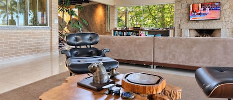 A modern living room with a leather chair, a wooden coffee table, and a television mounted on a stone wall.