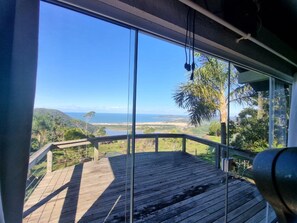 A wooden deck with a view of the ocean and hills. - Casa Garopaba Vista Panorâmica do Mar (Garopaba)