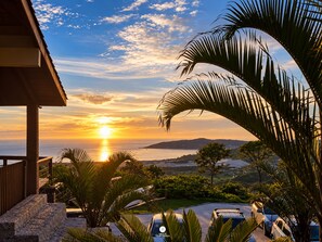 A sunset view from a balcony with a pool and palm trees. - Casa Garopaba Vista Panorâmica do Mar (Garopaba)