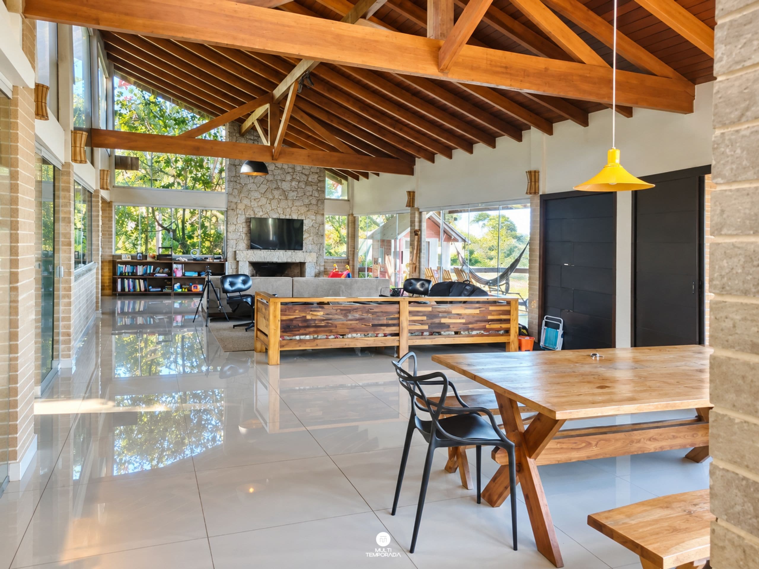 A spacious living area with a high ceiling, a stone fireplace, a large TV, and a dining table with chairs.