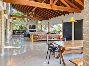 A spacious living area with a high ceiling, a stone fireplace, a large TV, and a dining table with chairs. - Casa Garopaba Vista Panorâmica do Mar (Garopaba)