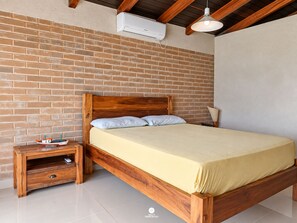 A bedroom with a wooden bed, a nightstand, a small table with a model ship, and a brick wall. - Casa Garopaba Vista Panorâmica do Mar (Garopaba)