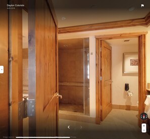 Puerta de madera que da a un área de ducha con piso de baldosas y un cuadro en la pared.
