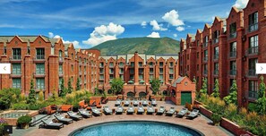 Un hotel con zona de piscina, varias sillas de descanso y montañas al fondo.