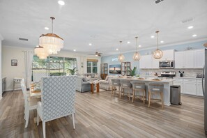 Een moderne keuken met witte kasten, een centraal eiland met barstoelen, hanglampen en uitzicht op de omgeving.