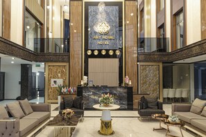 A spacious lobby with a reception desk, seating areas, and a chandelier.