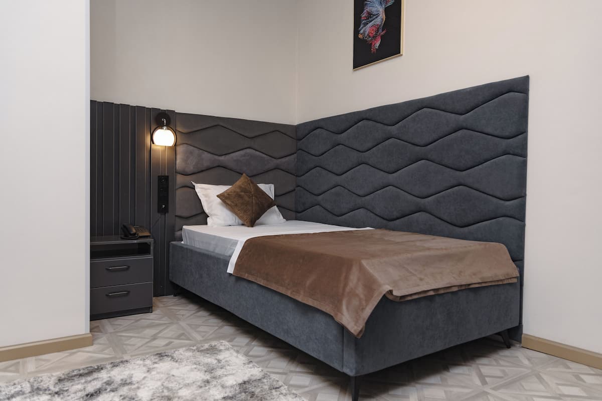 A modern bedroom with a grey upholstered bed, a nightstand with drawers, a wall-mounted lamp, and a patterned rug.