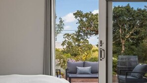 A bedroom with a large window, a bed, and a view of an outdoor patio with a sofa and a table. - Vineyard Haven: Pool, Hot Tub & Wine Country Charm (Kenwood)