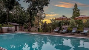 A swimming pool with lounge chairs and umbrellas, surrounded by trees and a sunset in the background. - Vineyard Haven: Pool, Hot Tub & Wine Country Charm (Kenwood)