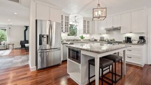 A modern kitchen with white cabinetry, stainless steel appliances, and a central island with stools. - Vineyard Haven: Pool, Hot Tub & Wine Country Charm (Kenwood)
