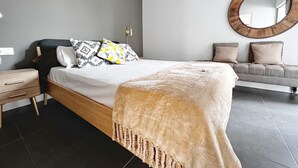 Een moderne slaapkamer met een groot bed, een nachtkastje, een sofa en een ronde spiegel aan de muur.