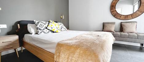A modern bedroom with a large bed, a bedside table, a sofa, and a round mirror on the wall.
