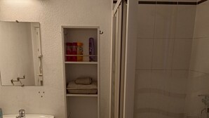 Een badkamer met een witte wastafel, een spiegel, een plank met toiletartikelen en een douchehoek.