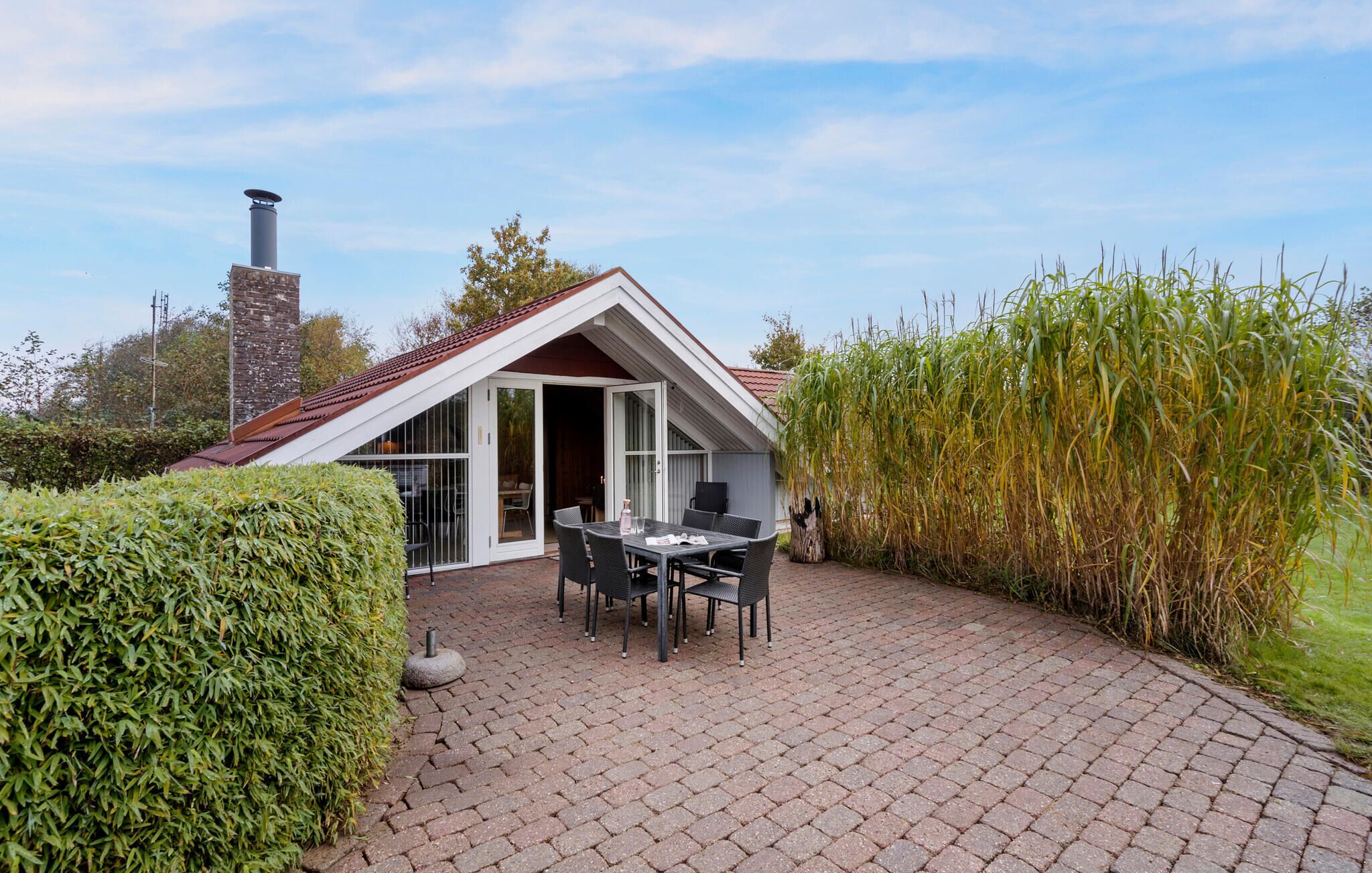 Ein Haus mit geneigtem Dach, einem Schornstein und einer Terrasse mit Tisch und Stühlen.