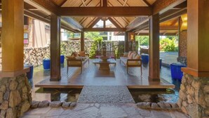 Un espace extérieur abrité, doté de piliers en pierre, d’un plancher en bois et offrant une vue sur un jardin et une piscine.