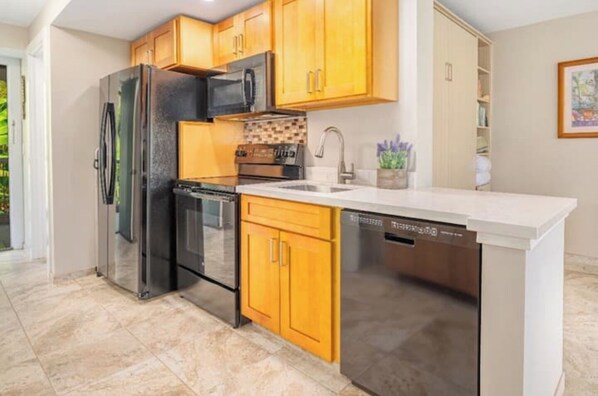 A modern kitchen with stainless steel appliances, wooden cabinets, and a white countertop.