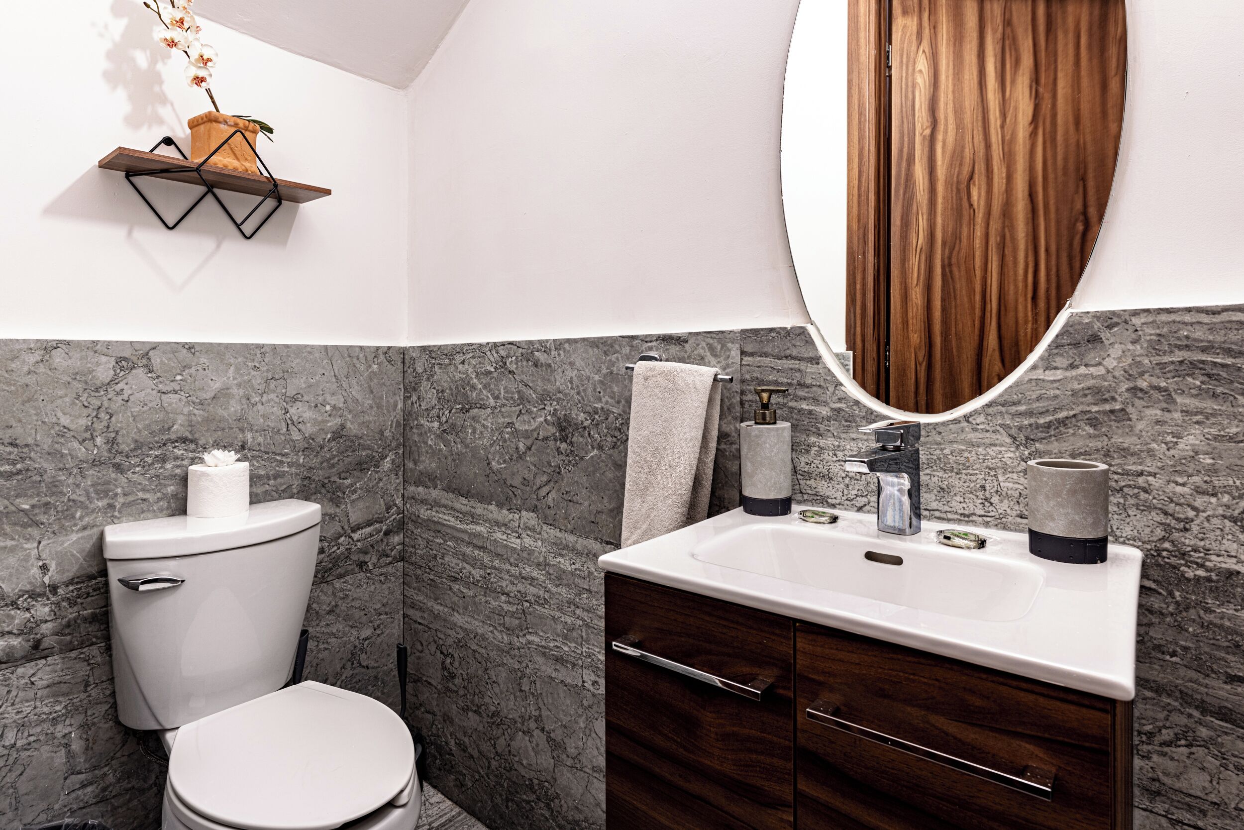 Een moderne badkamer met een marmeren wand, een houten wastafelmeubel, een toilet en een hangplant.
