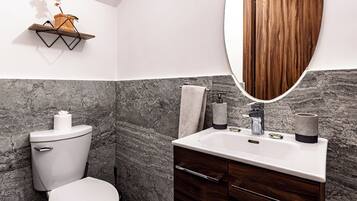 Een moderne badkamer met een marmeren wand, een houten wastafelmeubel, een toilet en een hangplant.