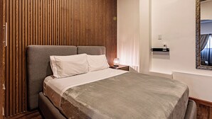 Un dormitorio moderno con pared de listones de madera, una cama tapizada en gris, una mesita de noche con lámpara y un espejo en la pared.