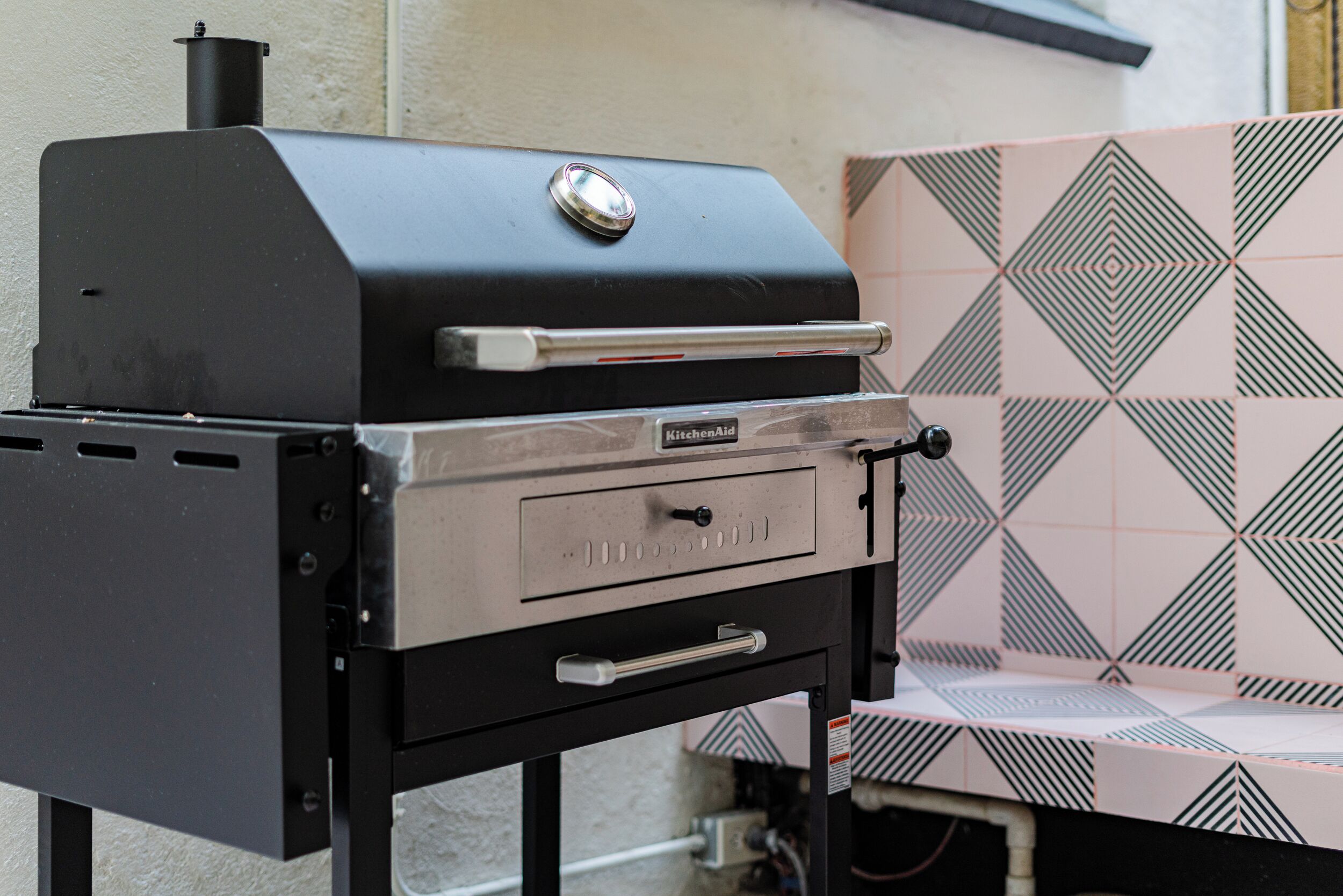 A black outdoor grill with a KitchenAid logo, a control panel, and a storage drawer.