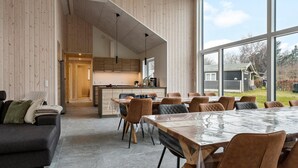A modern interior with a dining area, kitchen, and a large window offering a view of the outdoors. - Lovely home in Glesborg with sauna (Glesborg)