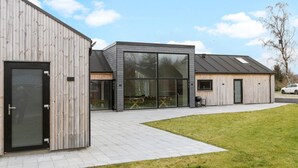 A modern building with large glass windows, a wooden facade, and a paved entrance area. - Lovely home in Glesborg with sauna (Glesborg)