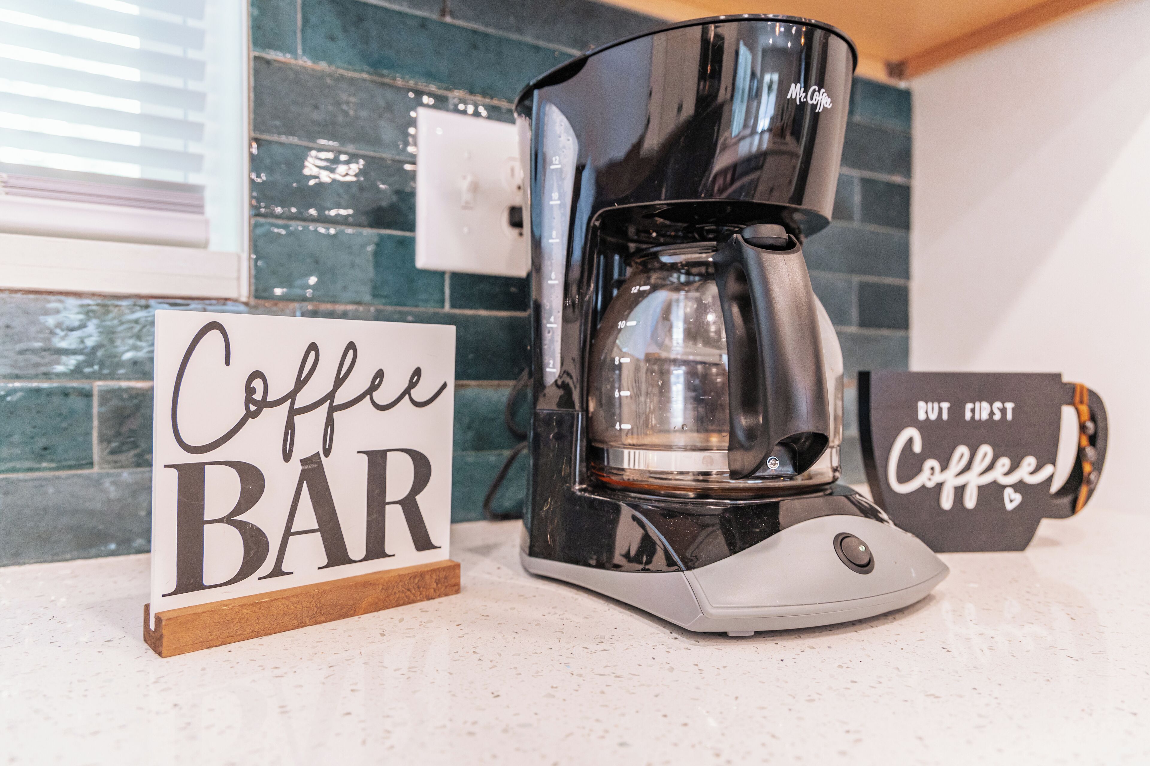 Een koffiezetapparaat op een aanrecht, met een bordje met de tekst 'Coffee BAR' en een ander bordje dat 'Eerst Koffie' zegt.
