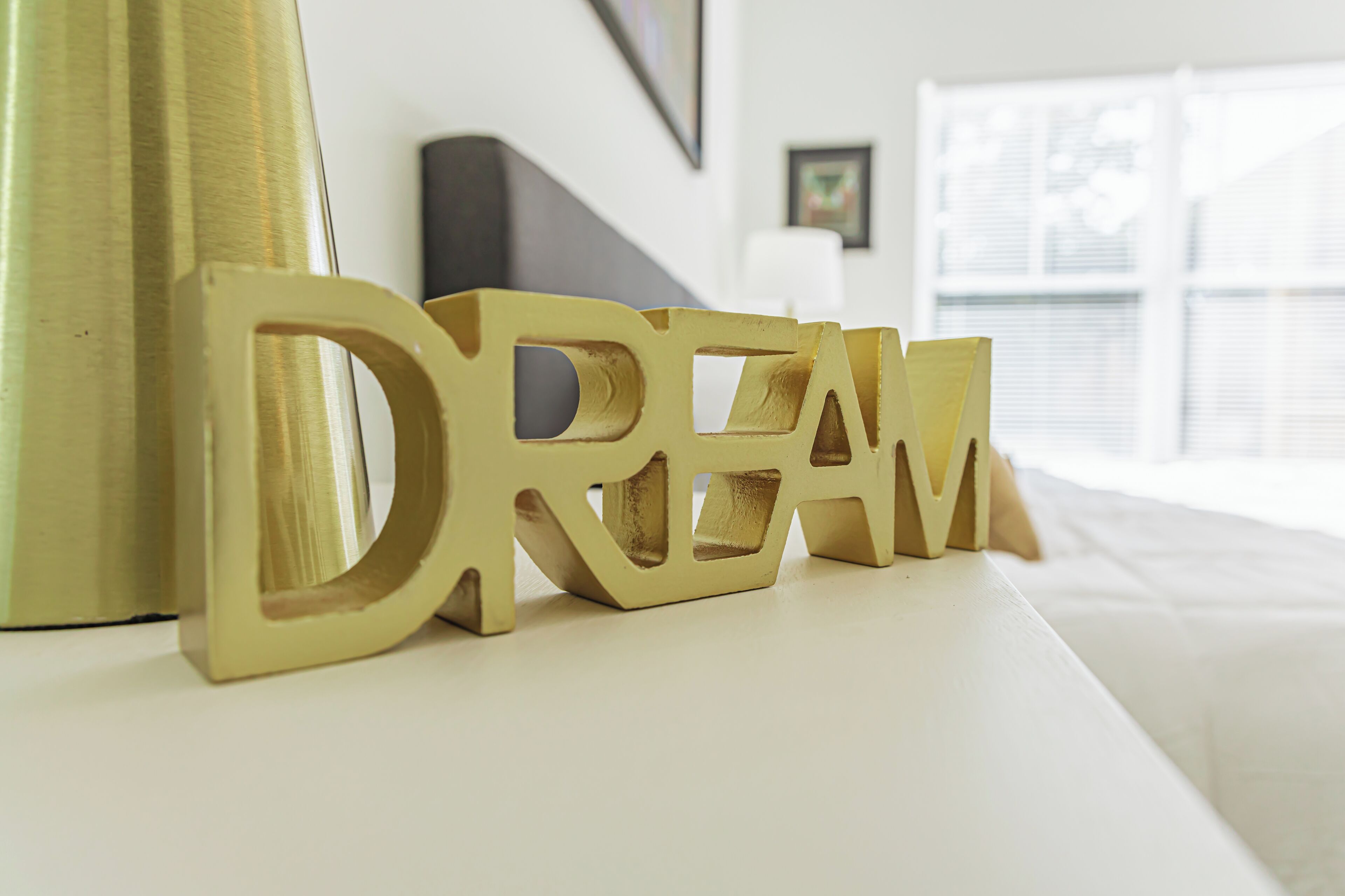 Un lit avec une tête de lit blanche et un panneau décoratif doré sur lequel est inscrit le mot « RÊVE ».