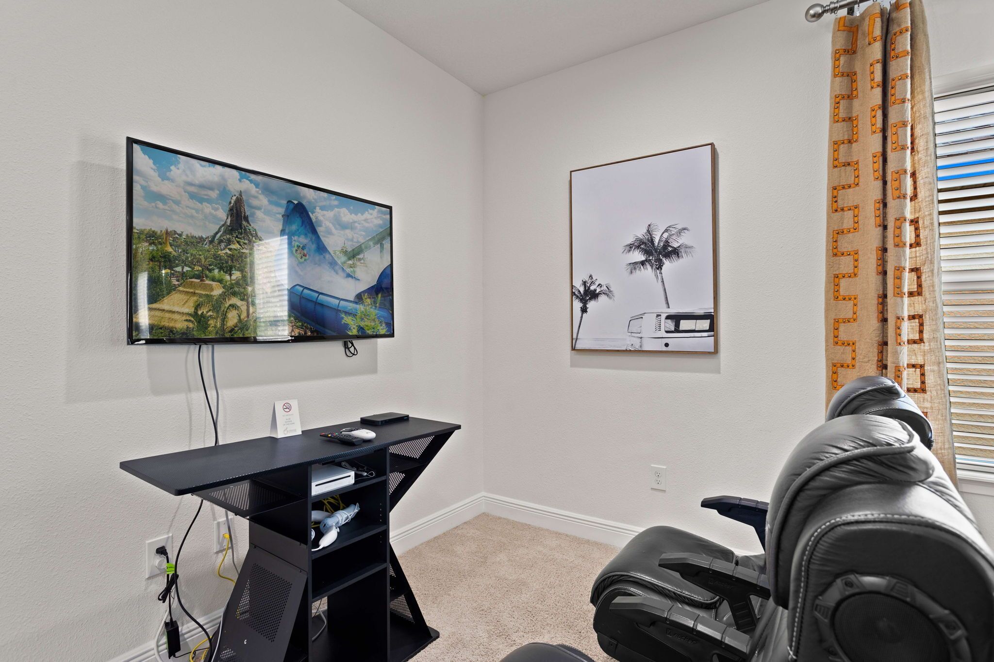 Een kamer met een wandtelevisie, een bureau met een computer en een bank.