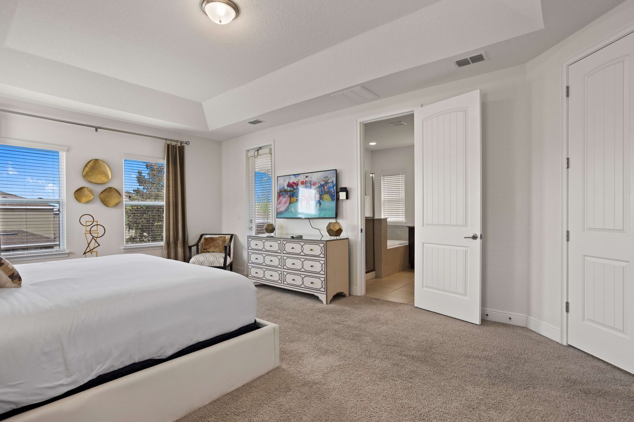 Un dormitorio con una cama grande, un aparador, un televisor y una puerta que da a otra habitación.