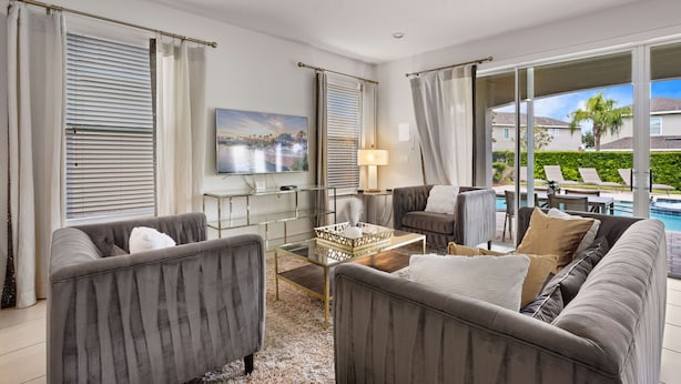 A modern living room with grey upholstered sofas, a glass coffee table, and a large flat-screen TV. - 5BR Spacious Villa • Pool, Spa • Near Disney (Kissimmee)