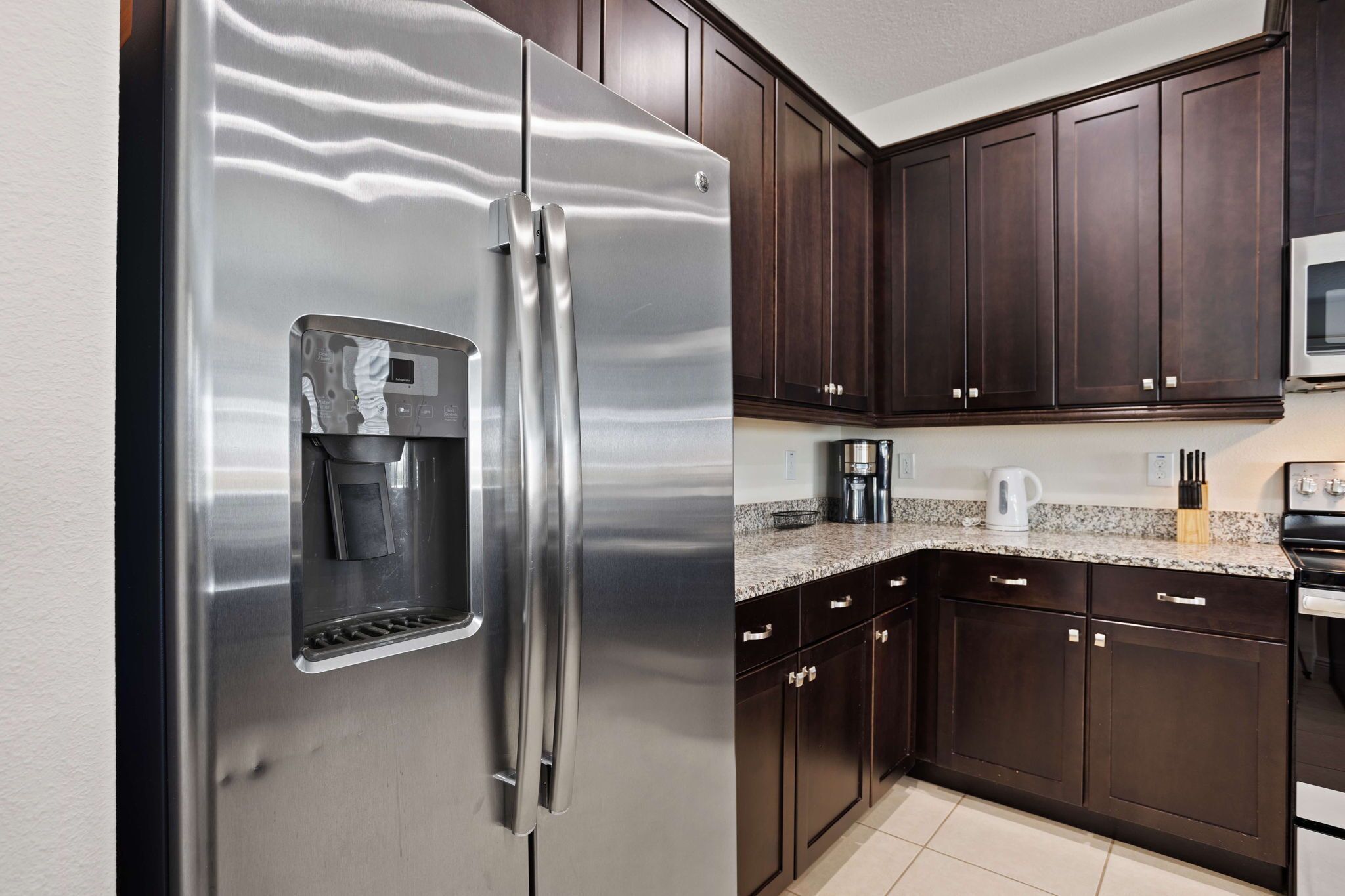 A kitchen with dark wooden cabinets, a stainless steel refrigerator, a microwave, and a granite countertop.