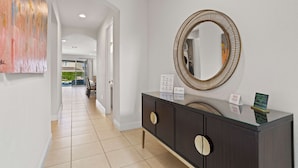 A modern hallway with a dark wooden console, a large mirror, and a welcome sign. - 5BR Spacious Villa • Pool, Spa • Near Disney (Kissimmee)