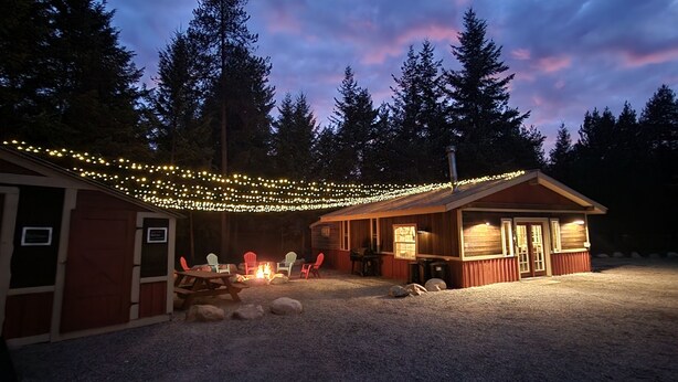 A cabin with a fire pit, outdoor seating, and string lights.