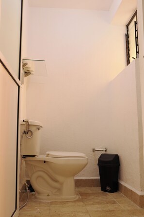 A small bathroom with a toilet, a trash bin, and a shower.
