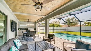 A covered outdoor area with a pool, seating, and a kitchen area. - Modern Home with Fenced In Yard (Cape Coral)