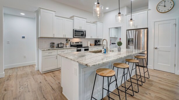 A modern kitchen with white cabinets, a large island with bar stools, stainless steel appliances, and pendant lighting. - Modern Home with Fenced In Yard (Cape Coral)