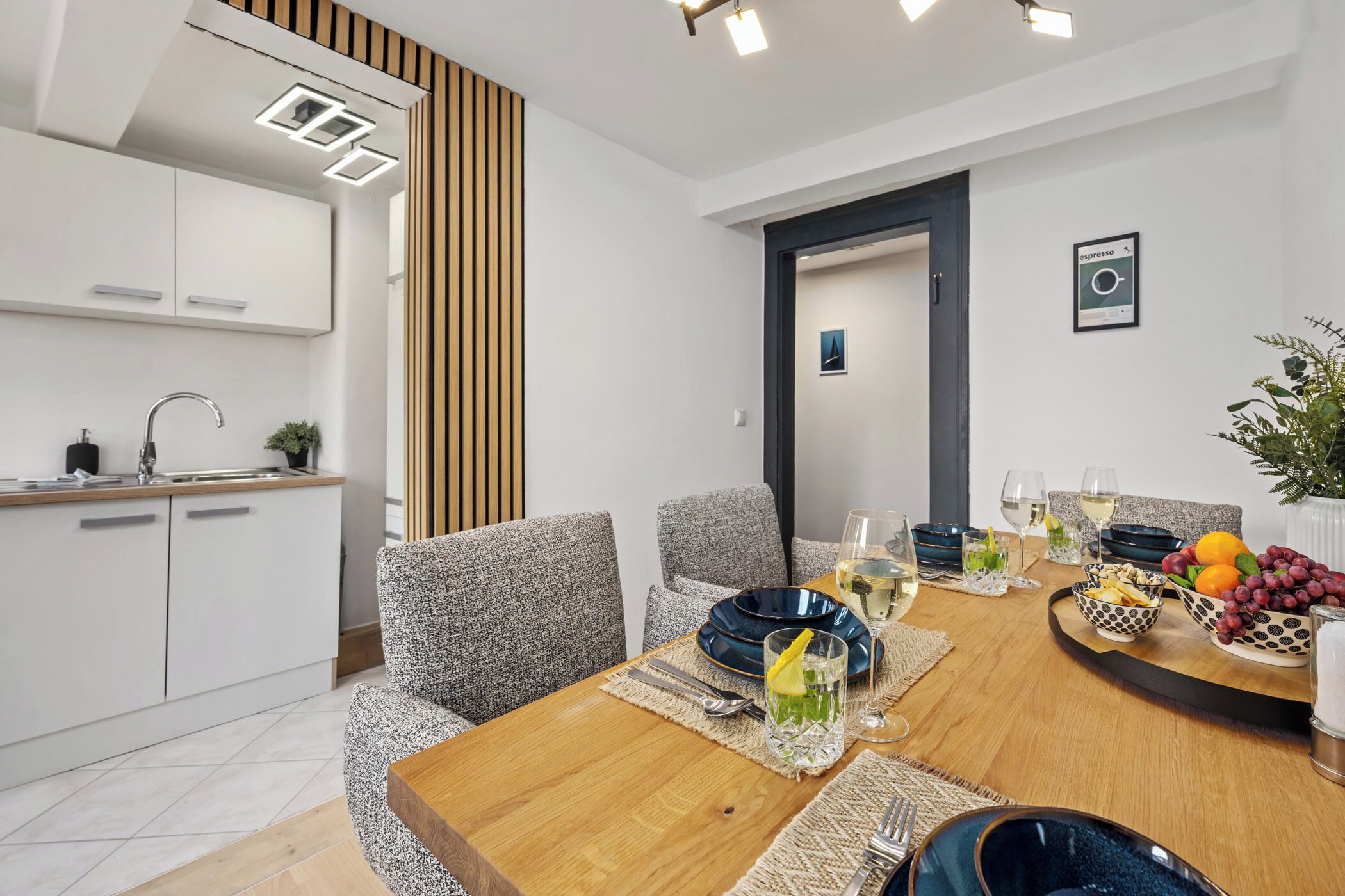 Un espace repas moderne avec une table en bois, des chaises à revêtement gris et une cuisine en arrière-plan.