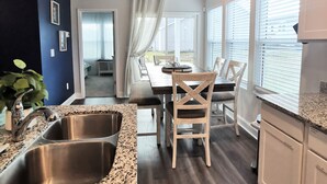 Una cocina moderna con encimeras de granito, fregaderos de acero inoxidable y un comedor con mesa y sillas de madera.
