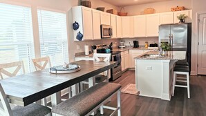Una cocina moderna con armarios blancos, una isla central y una zona de comedor con banco.