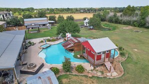 Une propriété résidentielle dotée d’une piscine, un bâtiment rouge avec un balcon, et une grande maison en arrière-plan.
